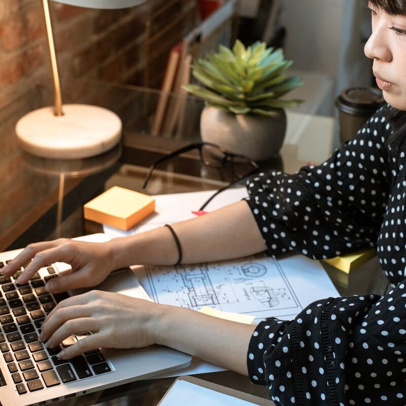 Focused woman wearing headphones, working on a laptop in a cozy home office setup with natural light.